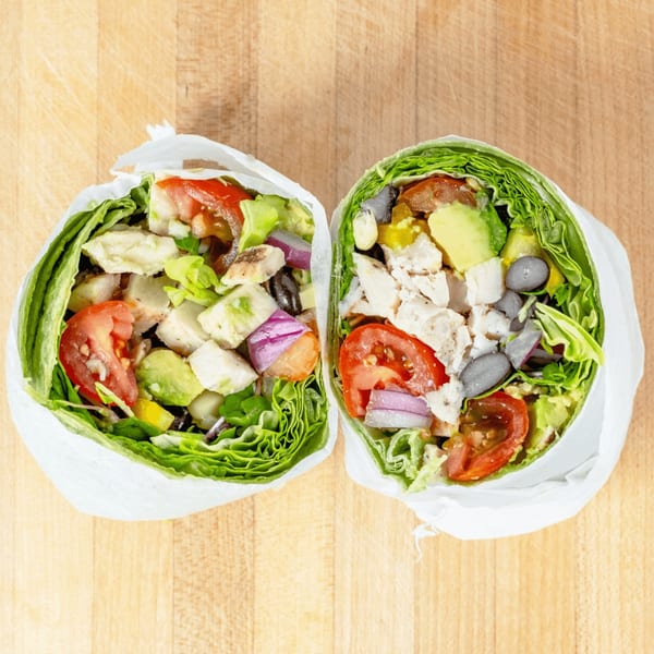 Two vibrant lettuce wraps, cut in half, filled with chicken, avocado, tomatoes, and black beans.