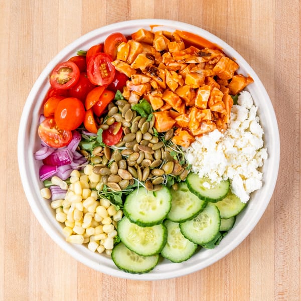 Overhead view of a colorful salad with chicken, tomatoes, corn, cucumbers, pumpkin seeds, and feta cheese.