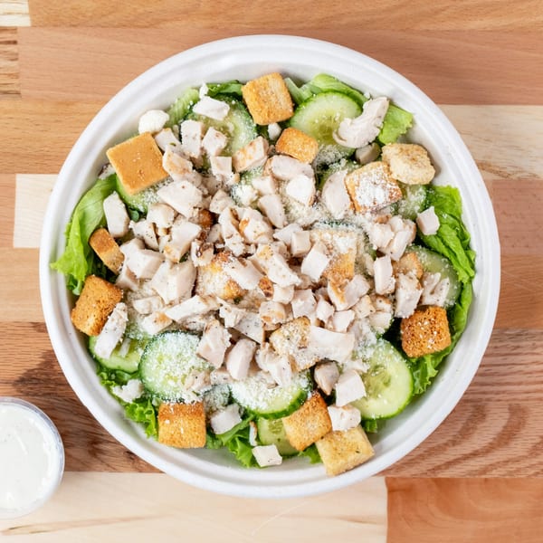 Overhead view of a chicken salad with lettuce, cucumbers, croutons, and parmesan cheese.