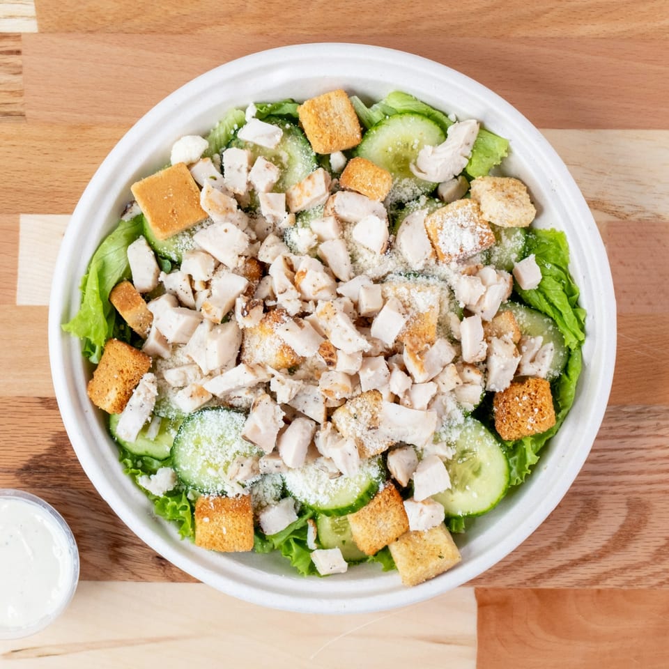 Overhead view of a chicken salad with lettuce, cucumbers, croutons, and parmesan cheese.