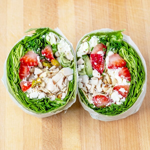 Two vibrant lettuce wraps filled with chicken, strawberries, feta, and green peppers on a wooden board.