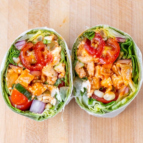 Two halves of a vibrant chicken and vegetable wrap, bursting with fresh ingredients on a wooden surface.