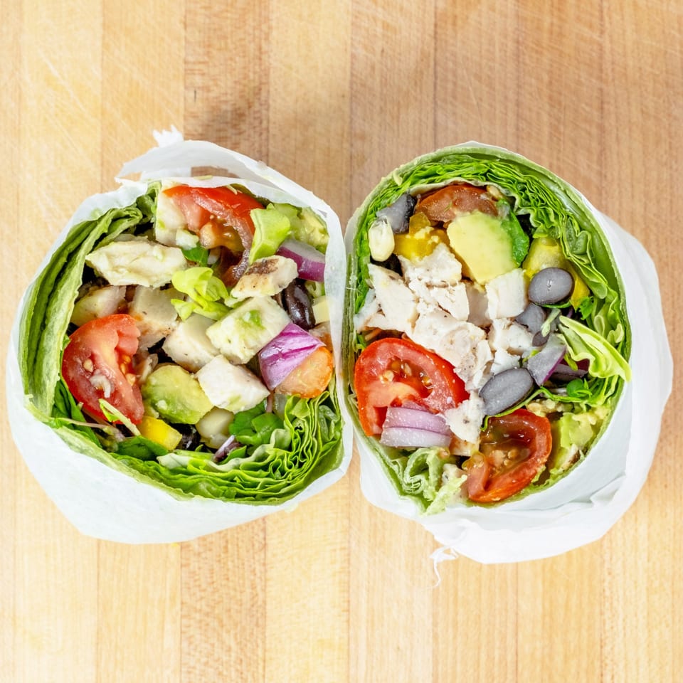 Two vibrant lettuce wraps filled with chicken, avocado, tomatoes, red onion, and black beans.