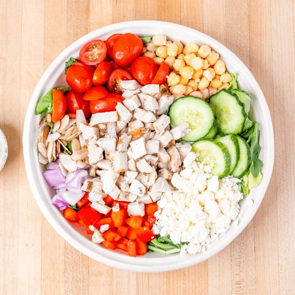 Overhead view of a colorful salad with chicken, tomatoes, chickpeas, cucumbers, and feta cheese.