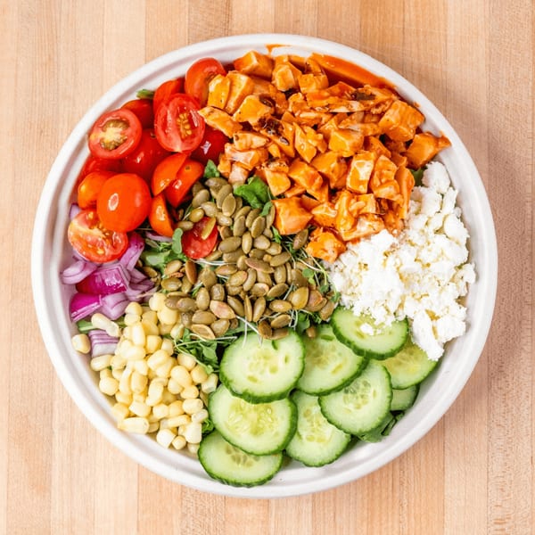 Overhead view of a colorful salad with chicken, tomatoes, feta, corn, cucumbers, and pumpkin seeds.
