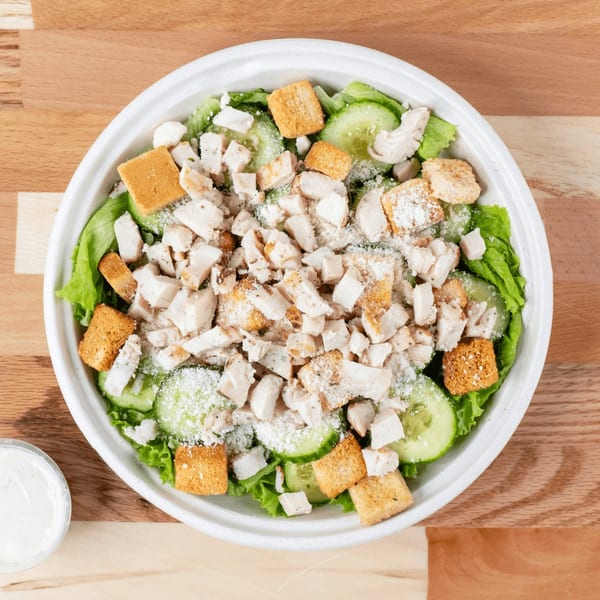 Overhead view of a chicken Caesar salad with croutons, cucumbers, and parmesan cheese.